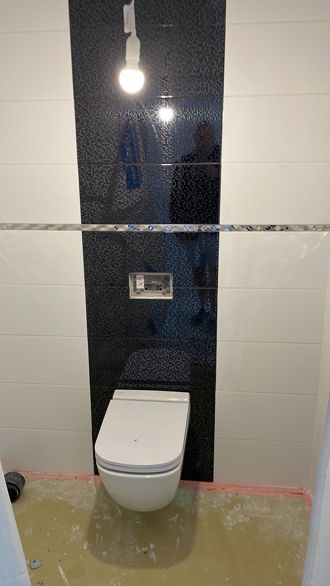 Podwieszana toaleta z czarno-białymi płytkami, widoczna instalacja podtynkowa, podłoga w trakcie prac wykończeniowych.