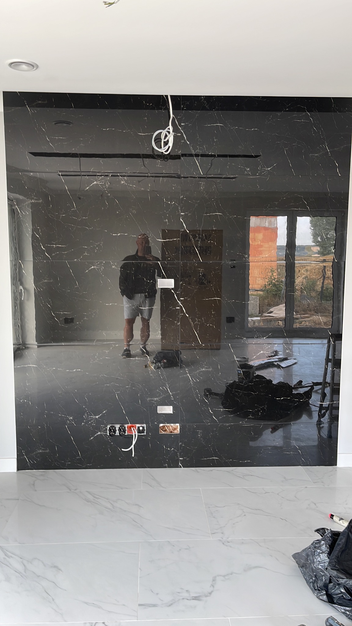 Montaż czarnej ściany z płytek imitujących marmur, widoczne gniazdka elektryczne i odbicie osoby robiącej zdjęcie.