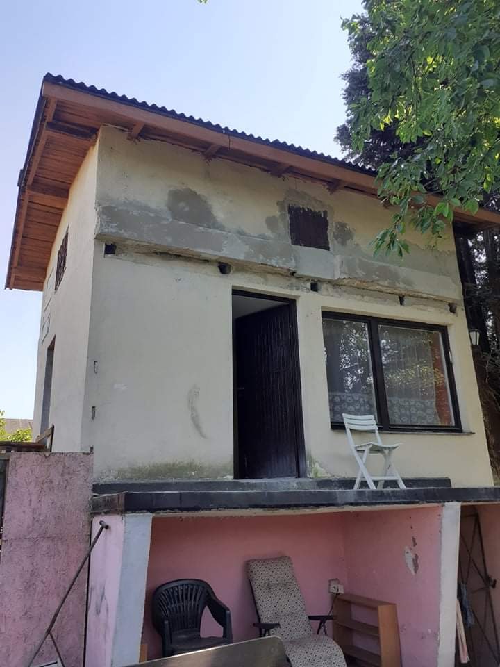 Niedokończony budynek z surowymi ścianami, drewnianym dachem i widocznym podpiwniczeniem, na balkonie białe krzesło.