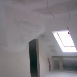 Poddasze w trakcie adaptacji: ściany i sufit po wstępnym szpachlowaniu, widoczne ślady po łatach, okno dachowe w skosie, wystające przewody elektryczne.