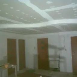 Wnętrze w trakcie prac wykończeniowych: sufit z płyt kartonowo-gipsowych, z widocznymi łączeniami i punktami mocowania, częściowo pokryty masą szpachlową, przygotowany do dalszej obróbki; trzy...