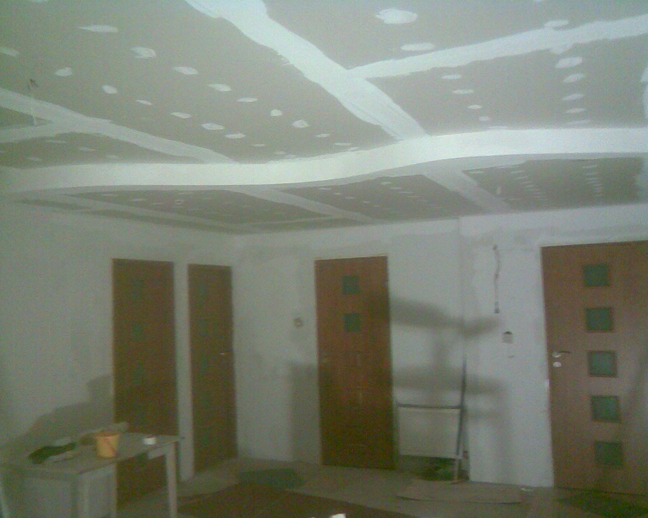 Wnętrze w trakcie prac wykończeniowych: sufit z płyt kartonowo-gipsowych, z widocznymi łączeniami i punktami mocowania, częściowo pokryty masą szpachlową, przygotowany do dalszej obróbki; trzy...