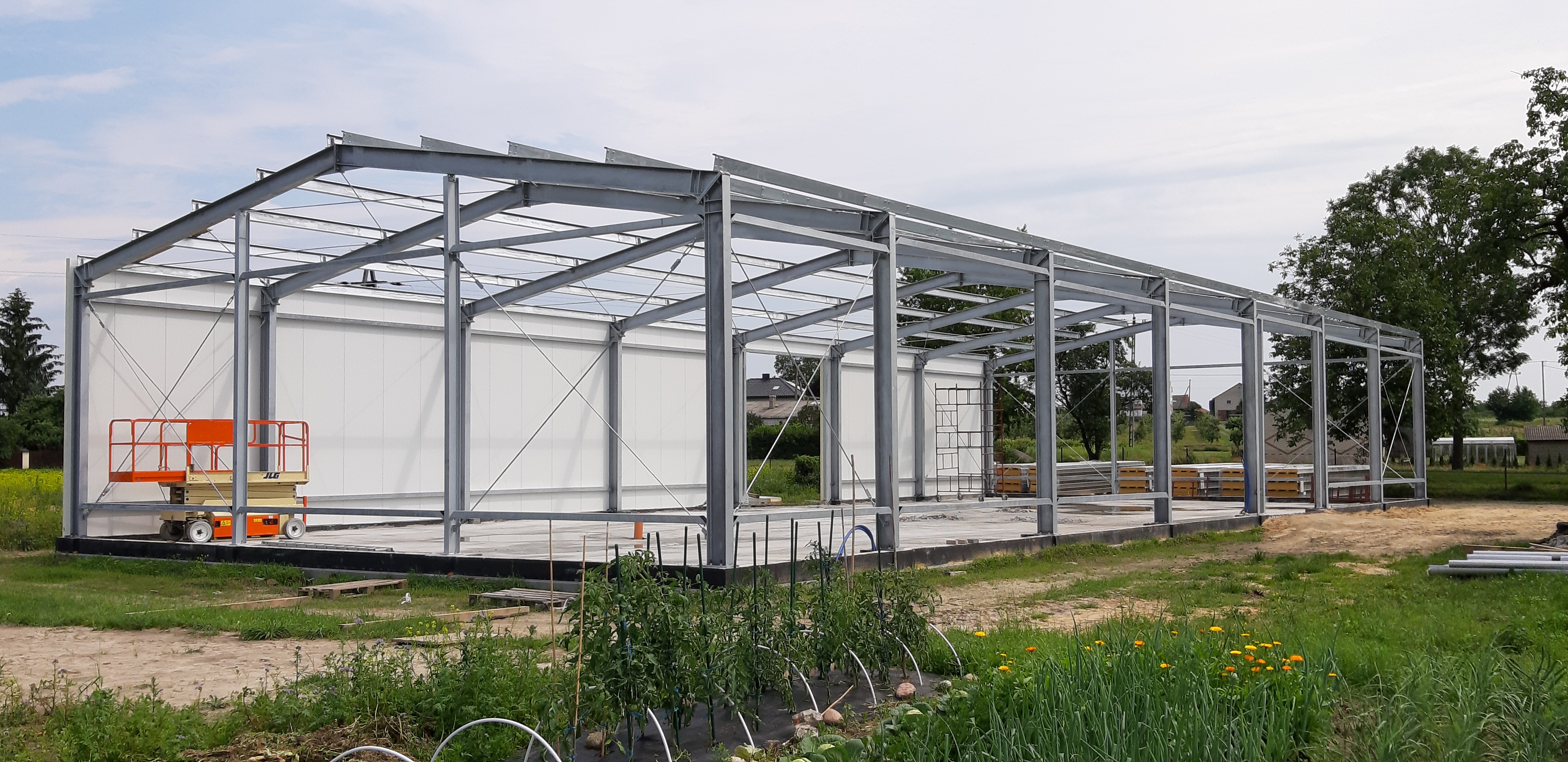 Konstrukcja stalowa hali w trakcie budowy w Firleju, widoczne zamontowane płyty warstwowe i podnośnik koszowy.