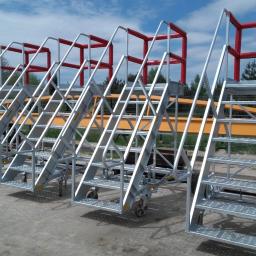 Zakład Techniczny NEVA Białystok - Mobilne schody metalowe z platformą, ocynkowane, z czerwoną barierką ochronną, na tle błękitnego nieba i zieleni drzew.