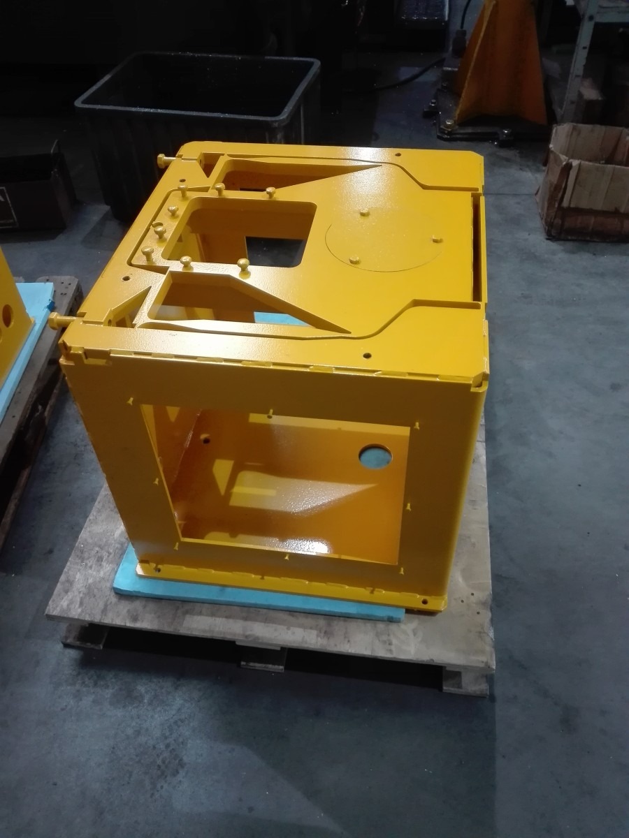 Żółta, pomalowana proszkowo, metalowa obudowa maszyny na palecie w hali produkcyjnej.