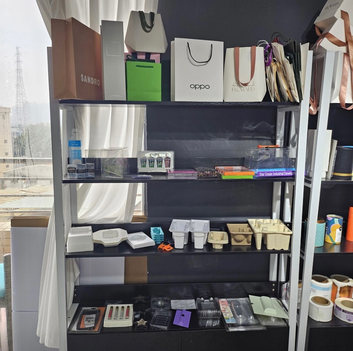 Regał z różnorodnymi torebkami papierowymi marek Sandro, Oppo i Floward oraz plastikowymi i papierowymi pojemnikami na różnych półkach, widok z boku.