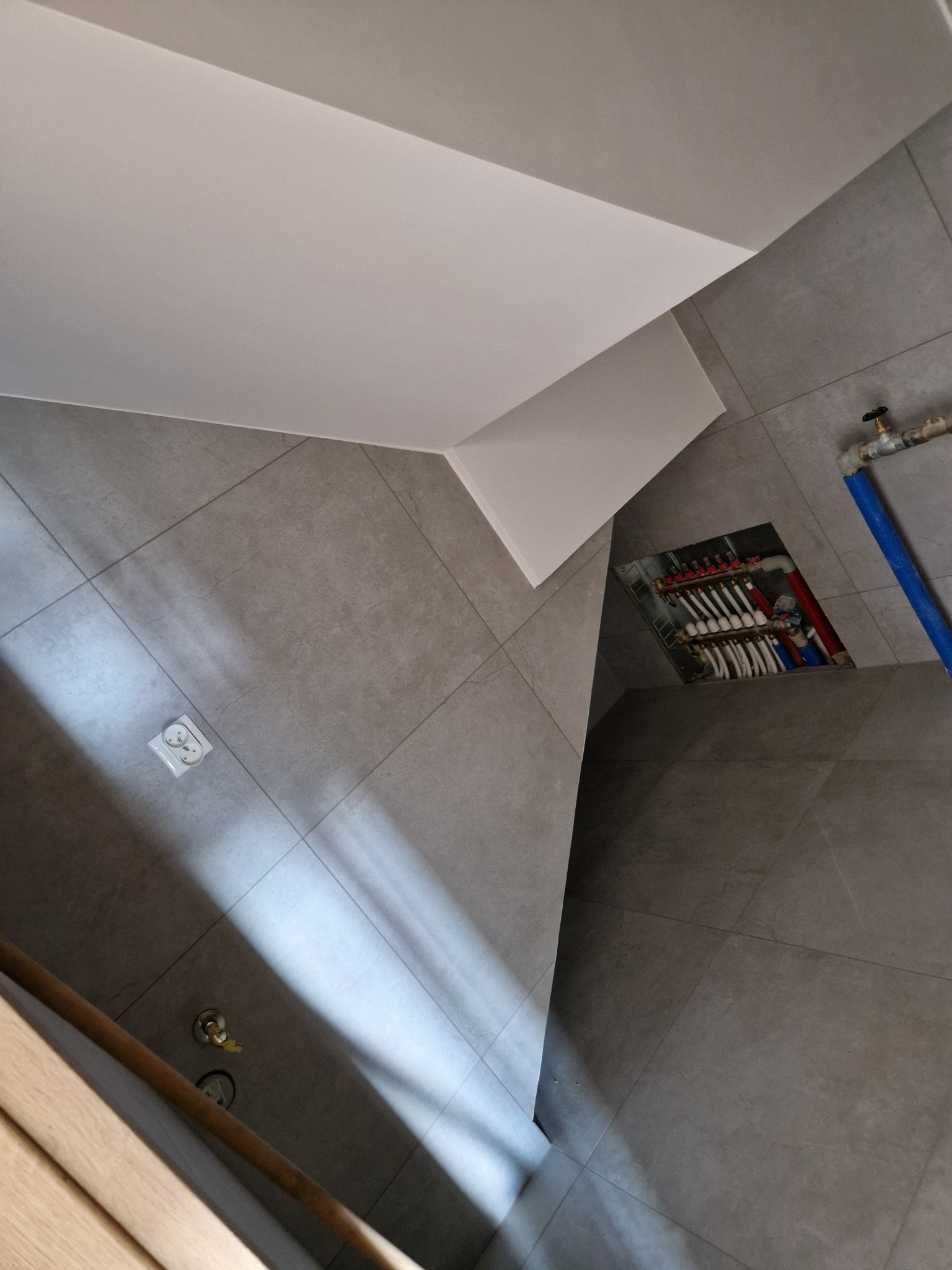 Szare płytki podłogowe i ścienne w łazience z widocznym fragmentem ogrzewania podłogowego w trakcie montażu oraz biały sufit podwieszany.