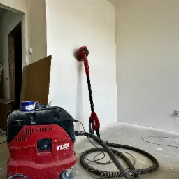 Wnętrze po szpachlowaniu: szlifierka teleskopowa Flex i odkurzacz przemysłowy Flex S 44 AC, gotowe do dalszej obróbki ścian. Jasne, gładkie powierzchnie.