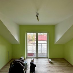 FINAL TOUCH DOMINIK PYDZIK - Pomalowane na zielono poddasze z oknem balkonowym. Widoczne puszki z farbą na drewnianej podłodze. Biały sufit i skosy.
