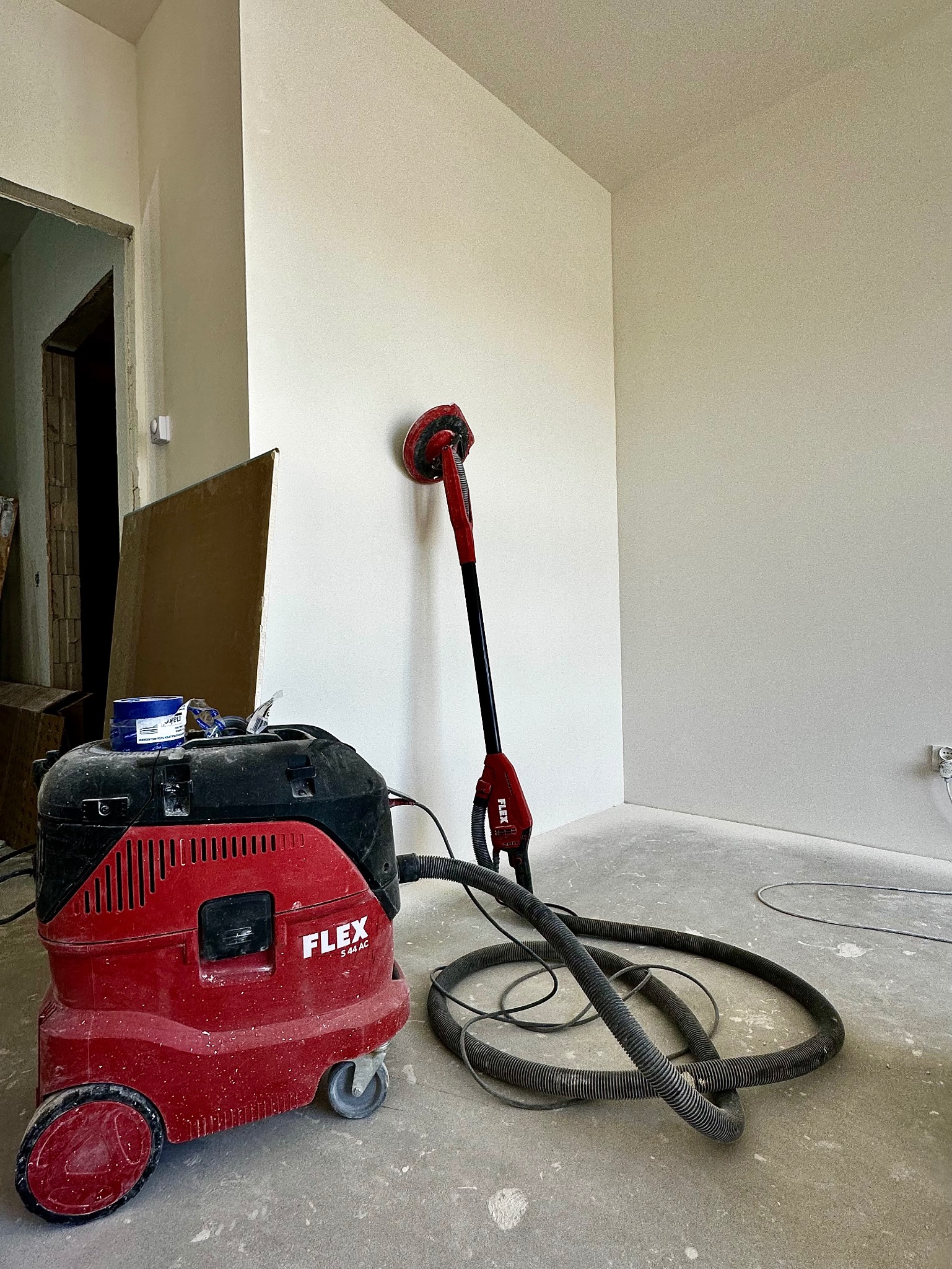 Wnętrze po szpachlowaniu: szlifierka teleskopowa Flex i odkurzacz przemysłowy Flex S 44 AC, gotowe do dalszej obróbki ścian. Jasne, gładkie powierzchnie.