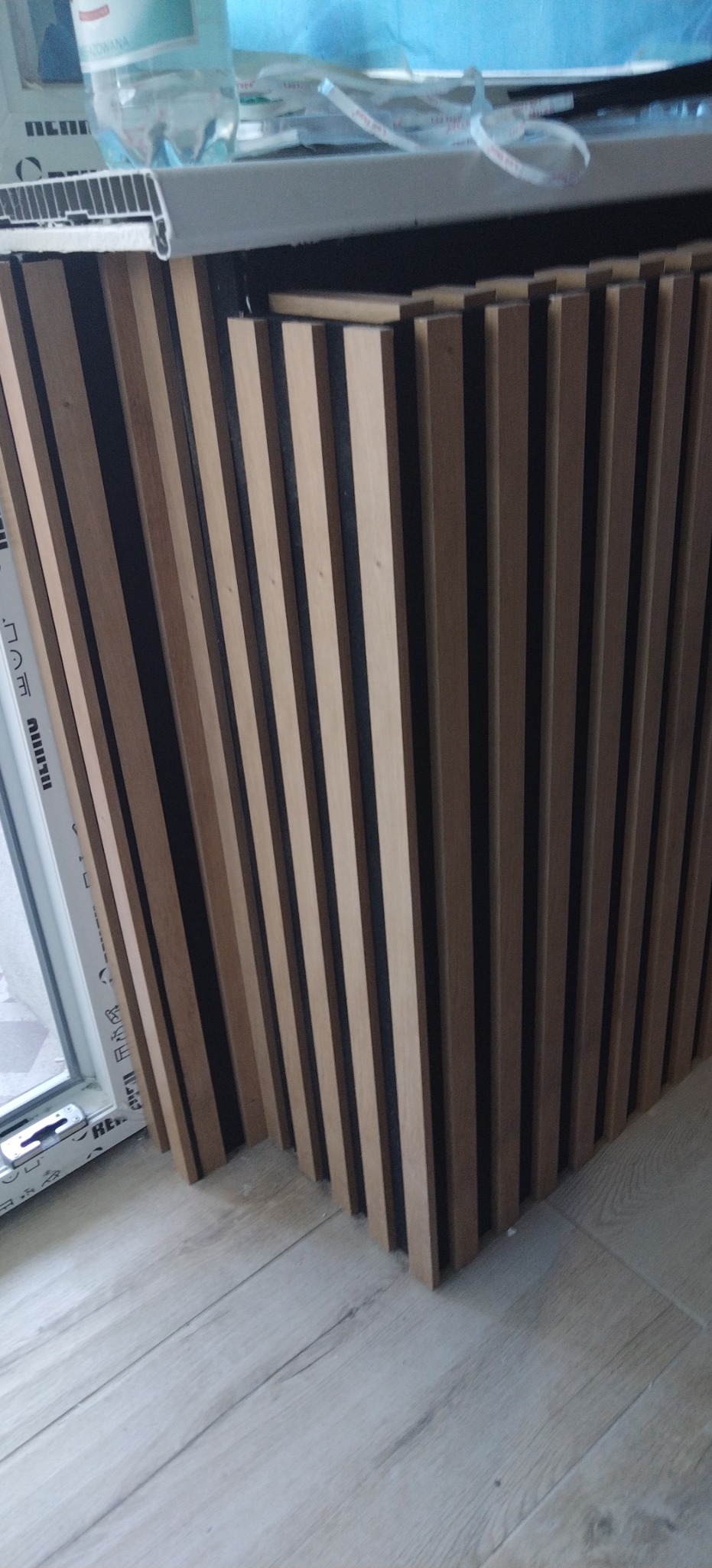 Drewniane panele ścienne z czarnymi wstawkami, zamontowane przy oknie, widoczne na tle jasnej podłogi.