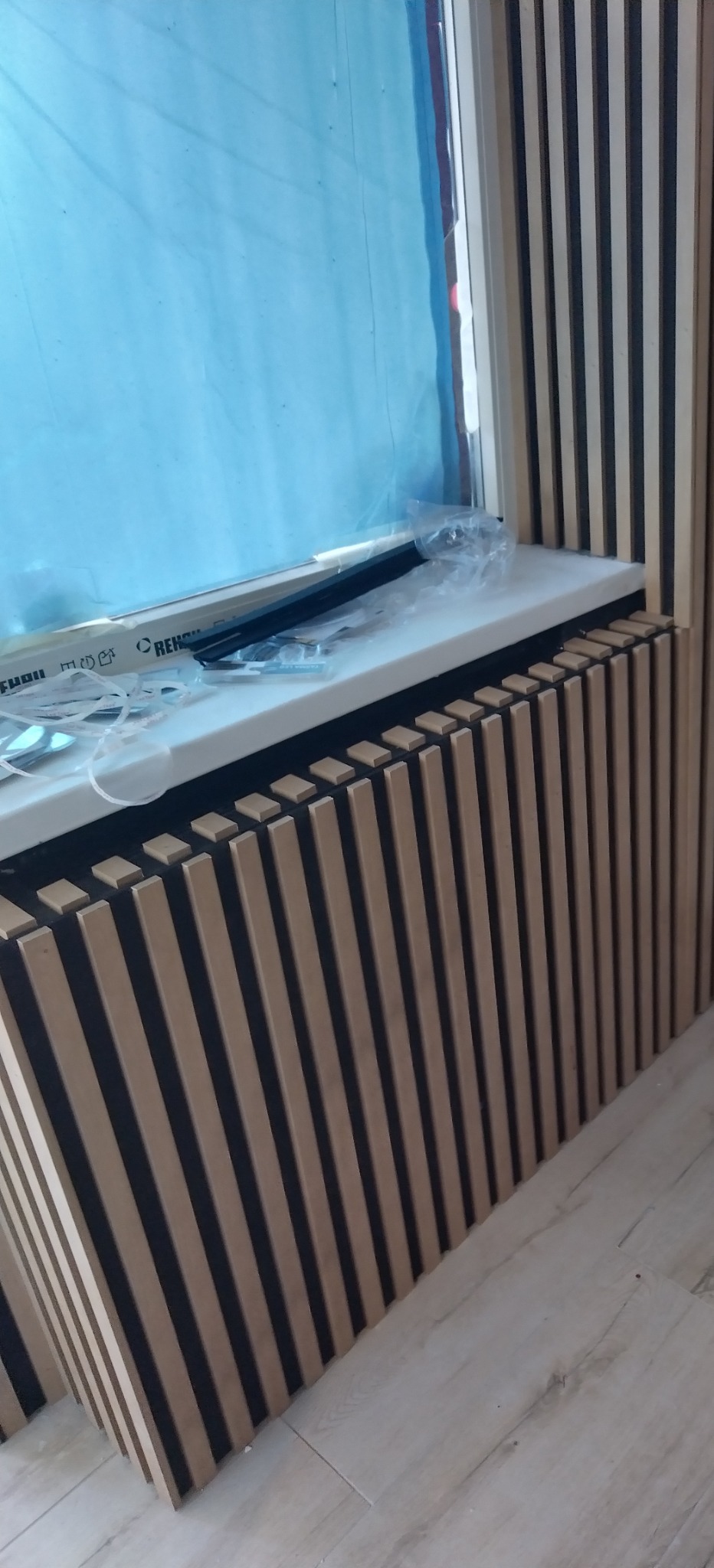 Montaż paneli dekoracyjnych ściennych z MDF przy oknie, widoczne folie ochronne na oknie i akcesoria montażowe na parapecie.