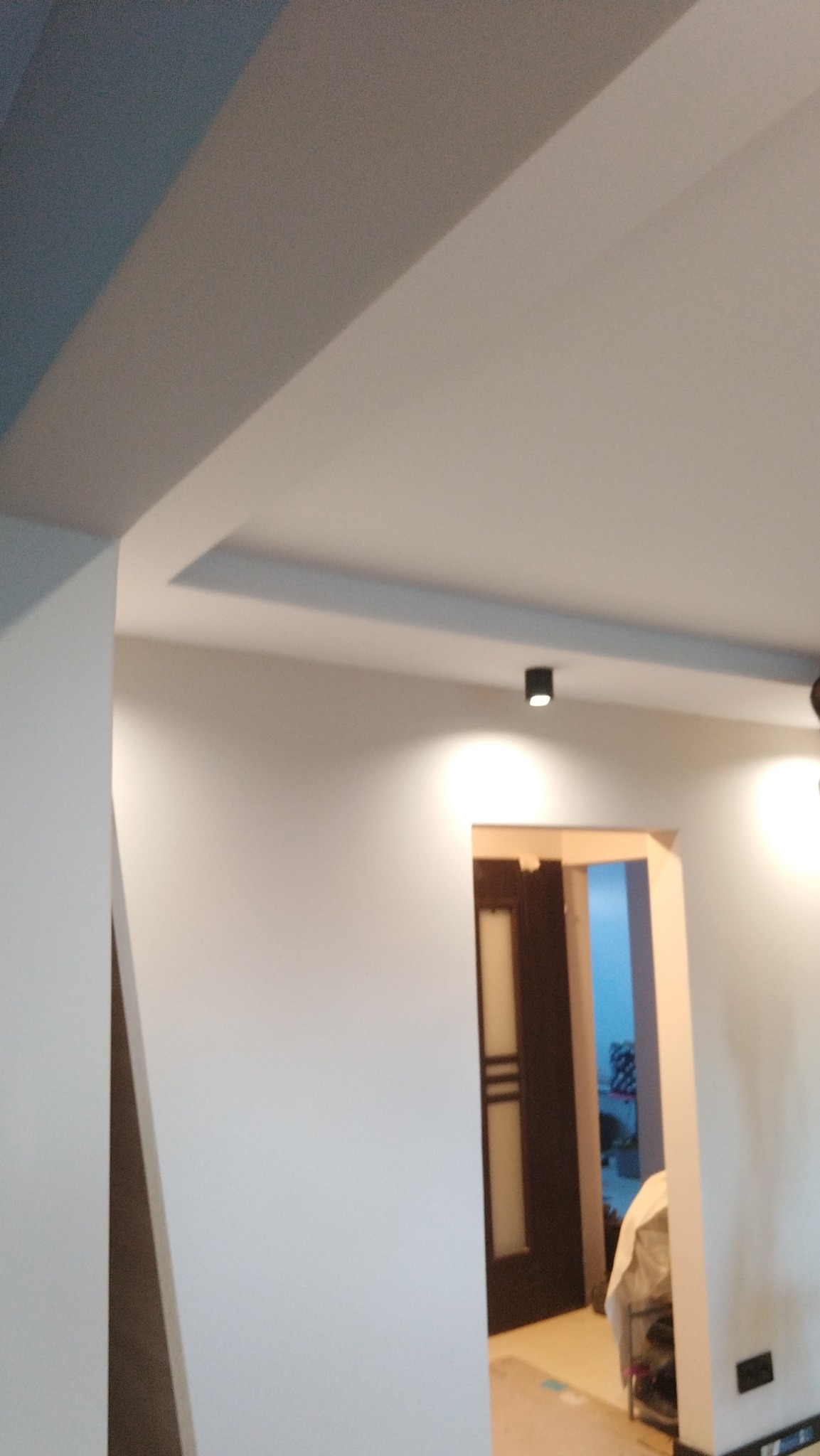 Wnętrze po remoncie: gładkie, białe ściany, sufit z podwieszanym elementem i oświetleniem punktowym, widoczny fragment drzwi i pomieszczenia w głębi.