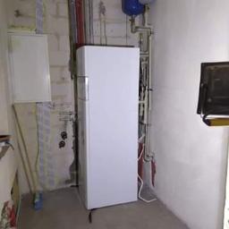 Daminstal - Biały piec gazowy kondensacyjny z dwoma zbiornikami wyrównawczymi na ścianie, w surowym pomieszczeniu z widocznymi instalacjami i elementami wykończeniowymi.