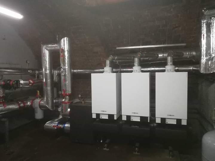 Trzy białe piece gazowe marki Viessmann zamontowane w piwnicy z ceglanym sklepieniem, widoczne rury w izolacji.