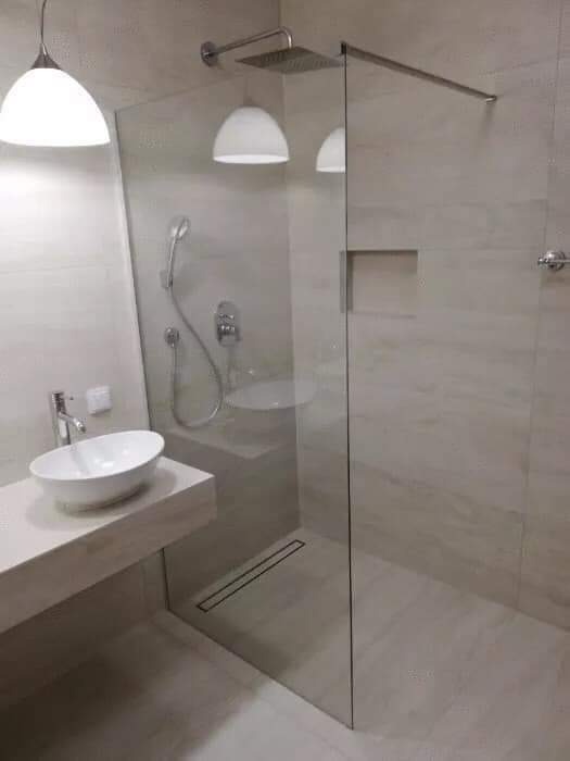 Nowoczesna łazienka z kabiną prysznicową typu walk-in, umywalką nablatową na blacie z płytek imitujących marmur i podwieszanymi lampami.