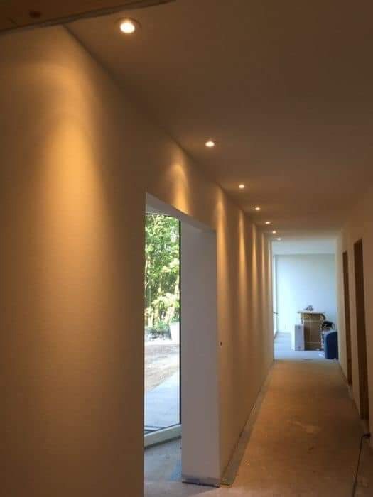 Korytarz w trakcie wykańczania z równo wyszpachlowanymi ścianami, oświetleniem punktowym w suficie i widoczną szarą podłogą w stanie surowym.