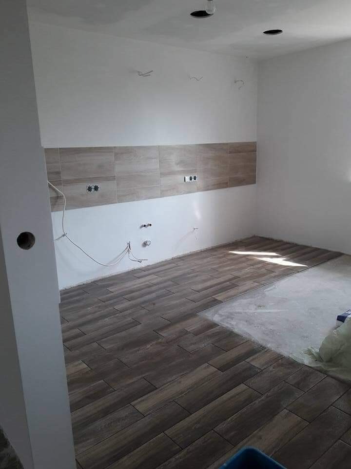 Układanie podłogi z płytek imitujących drewno w nowym pomieszczeniu, widoczne gniazdka elektryczne na ścianie i fragment nieukończonej podłogi.