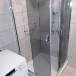 Szczegółowe ujęcie kabiny prysznicowej z chromowanymi elementami w łazience w Szczecinie, obok widoczna biała pralka.