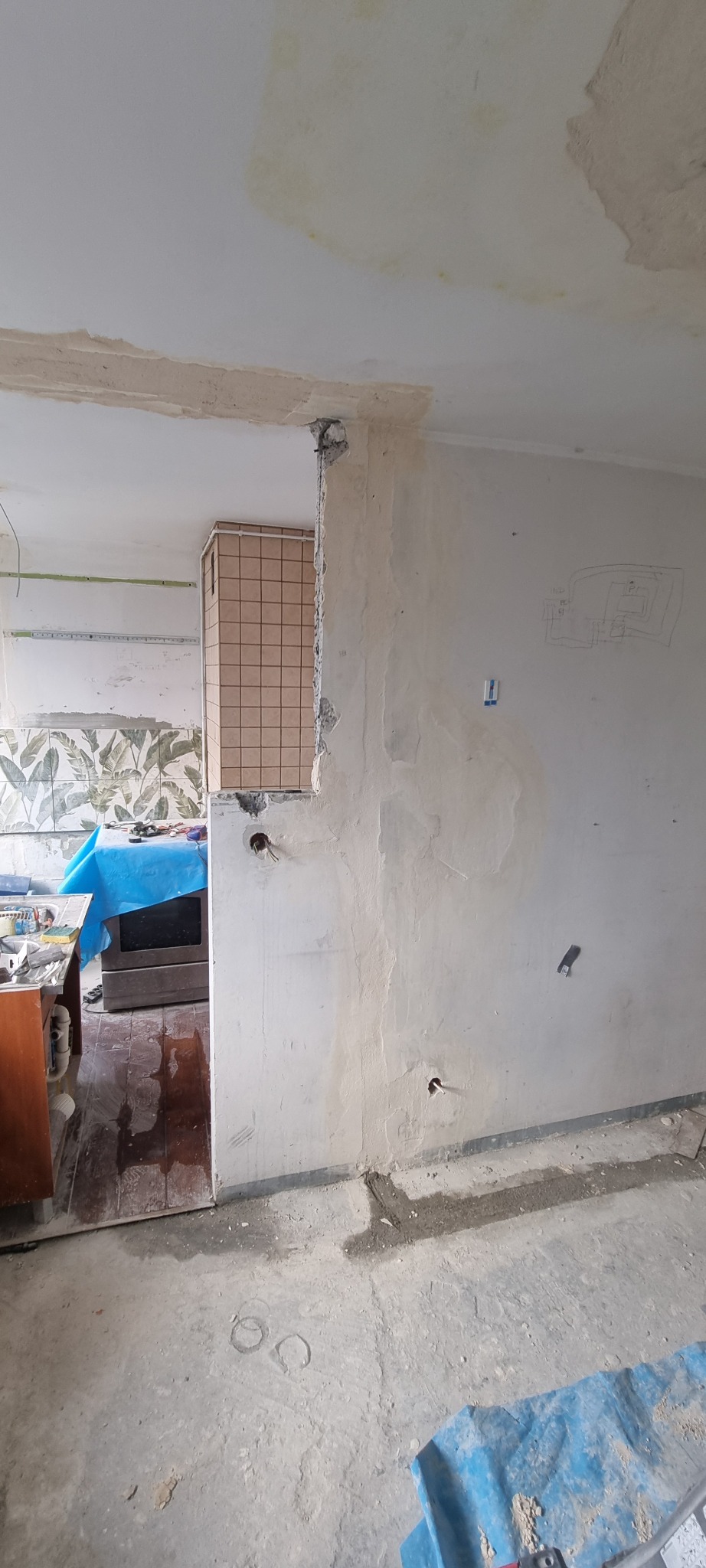 Wnętrze w trakcie remontu: odkryte przewody elektryczne w ścianie, fragment ściany obłożony płytkami, nieukończona instalacja elektryczna, na ścianie schemat instalacji elektrycznej.