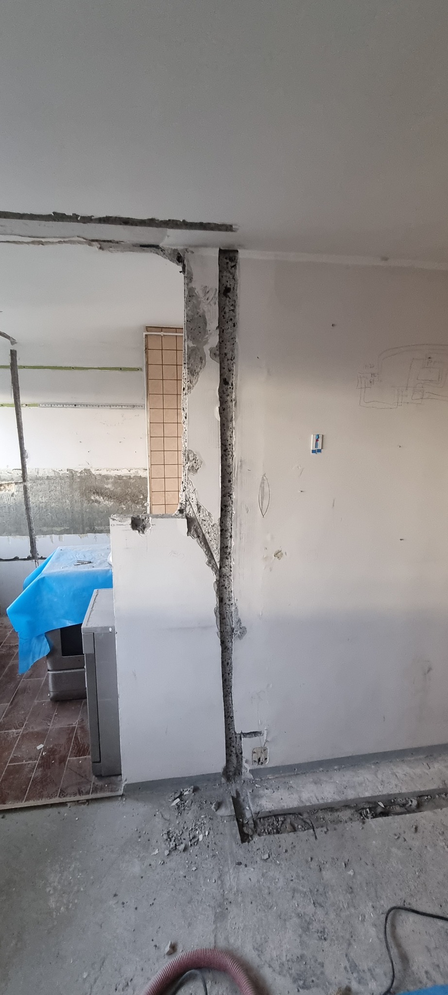 Wykute bruzdy w ścianie i suficie pod przewody elektryczne, widoczne przewody w ścianie i schemat instalacji elektrycznej narysowany na ścianie, gruz na podłodze.