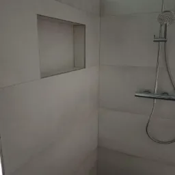 Wykończona kabina prysznicowa z szarymi, poziomymi płytkami, wnęką w ścianie i chromowaną deszczownicą.