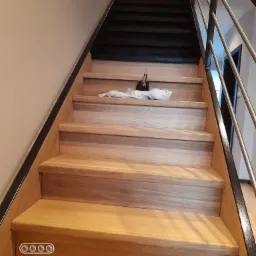 Drewniane schody z metalową balustradą, widok z dołu, na jednym ze stopni leżą ścierki i puszka, schody prowadzą na wyższą kondygnację.