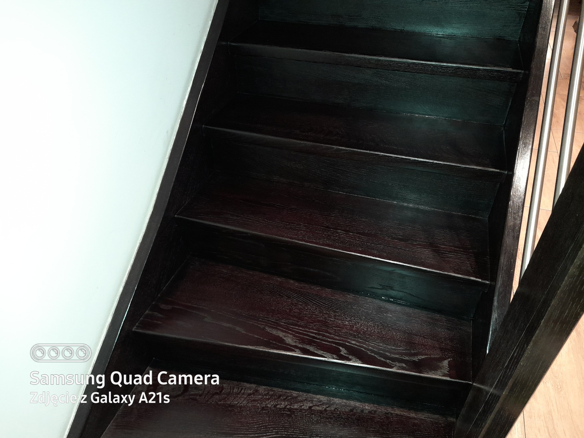 Drewniane schody o ciemnym wybarwieniu z metalową poręczą, widok z dołu, oświetlenie mieszane.