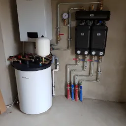 Nowoczesna kotłownia z piecem gazowym Vaillant, zbiornikiem buforowym i rozdzielaczami, rury miedziane i stalowe, manometry, instalacja po montażu, surowy beton na ścianach i posadzce.