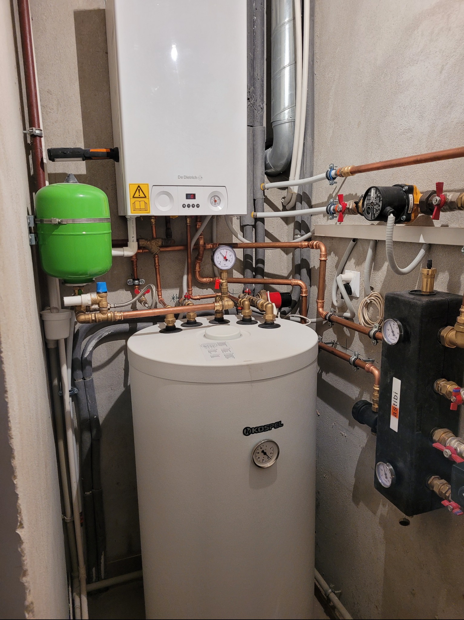 Zestaw kotła gazowego De Dietrich z zasobnikiem Kospel i zielonym naczyniem przeponowym, połączony miedzianą instalacją w pomieszczeniu technicznym.