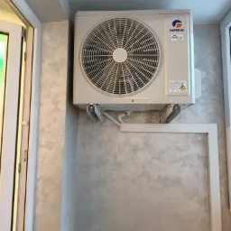 Zamontowana jednostka zewnętrzna klimatyzacji Gree Inverter na wspornikach, widoczne szare ściany z efektem betonu.