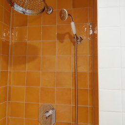 DAR - MAX DARIUSZ NAPIÓRKOWSKI - Wykończona kabina prysznicowa z pomarańczowymi i białymi płytkami, chromowaną armaturą i deszczownicą. Widoczny detal: ośmiokątny panel sterowania.