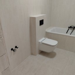 DAR - MAX DARIUSZ NAPIÓRKOWSKI - Jasna łazienka po remoncie: beżowe płytki, podwieszana toaleta z czarnym przyciskiem, bateria wannowa. Minimalistyczny design, świeżo wykończone wnętrze.