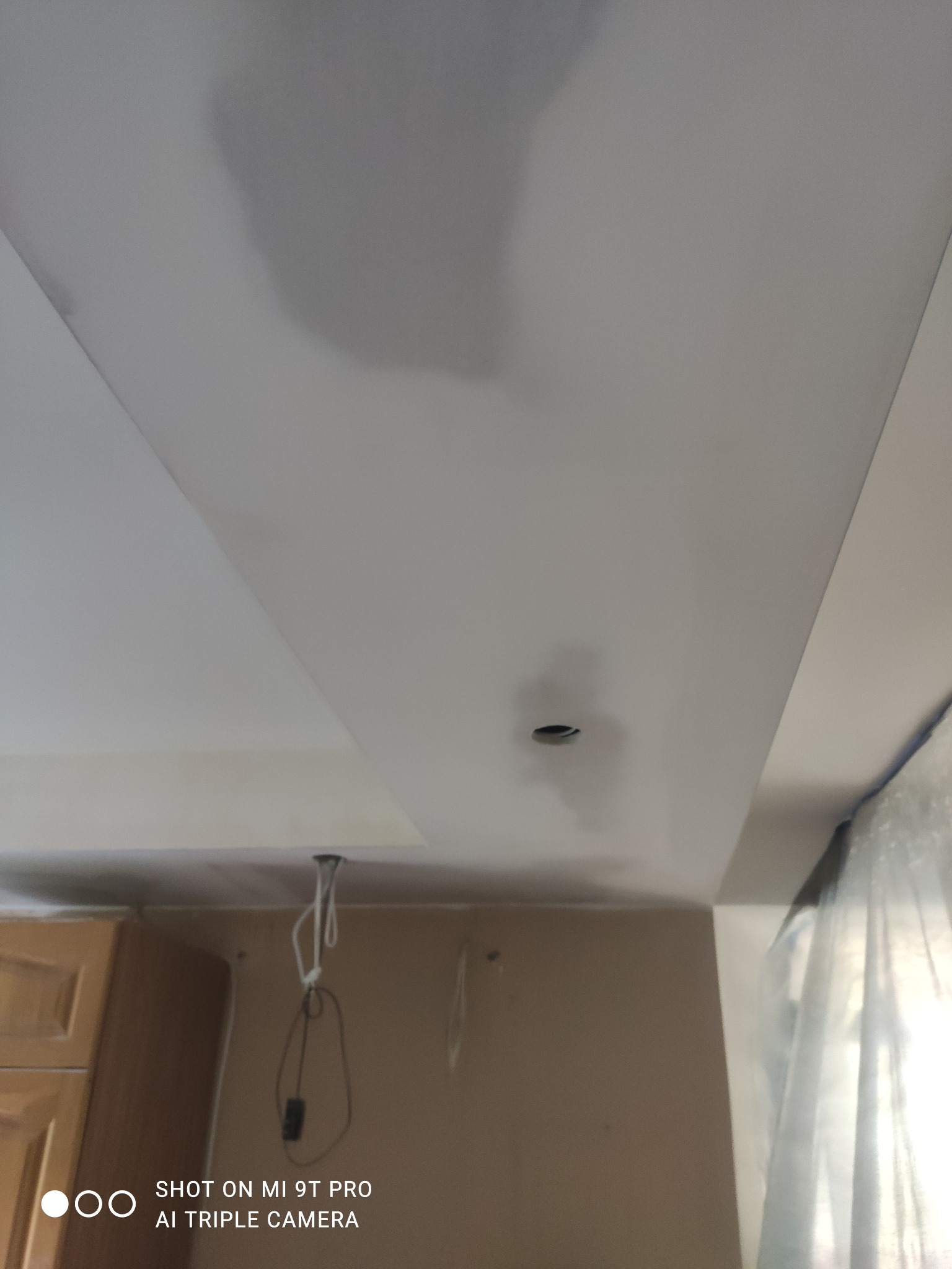 Niedokończony sufit podwieszany z płyty gipsowo-kartonowej z widocznymi śladami szpachlowania i otworem na oświetlenie, widoczne wiszące kable i fragment szafki kuchennej.