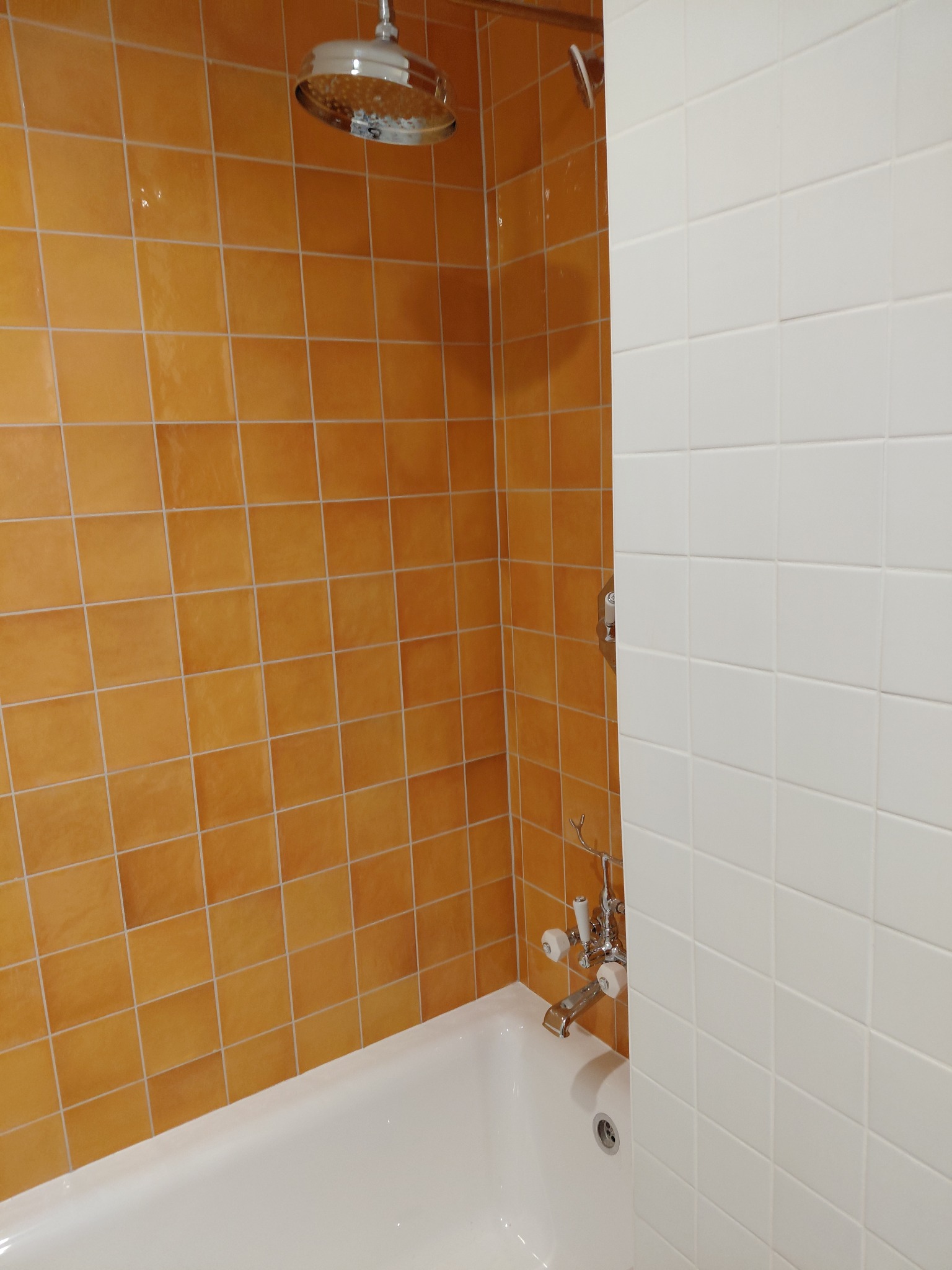 Wykończona kabina prysznicowa z pomarańczowymi i białymi kwadratowymi płytkami, chromowaną armaturą i białą wanną. Widok z góry na głowicę prysznicową.