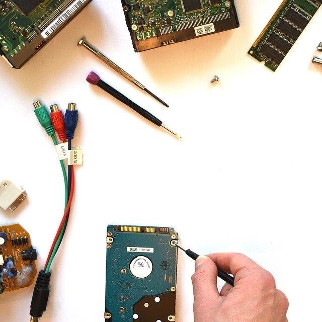 Otwieranie dysku twardego śrubokrętem na białym tle, widoczne inne podzespoły komputerowe i kable.