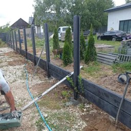 Artblok - Montaż ogrodzenia kompozytowego: widoczne słupki i deski w trakcie instalacji, narzędzia pracy, częściowo ukończony fragment ogrodzenia na tle zieleni.