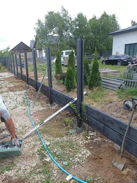 Montaż ogrodzenia kompozytowego: widoczne słupki i deski w trakcie instalacji, narzędzia pracy, częściowo ukończony fragment ogrodzenia na tle zieleni.