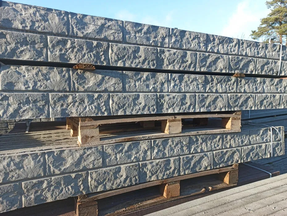 Ułożone na paletach bloczki betonowe imitujące kamień, przeznaczone do budowy ogrodzenia. Widoczne detale faktury i nieregularny kształt bloczków.