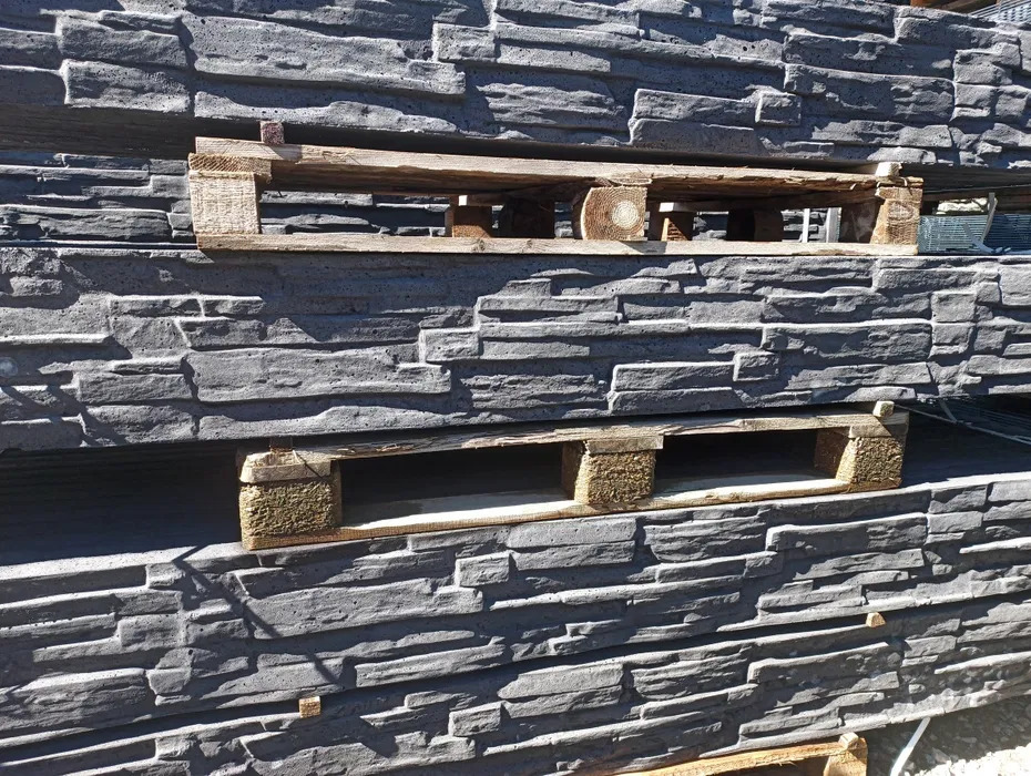 Szare panele imitujące kamień ułożone na paletach, widoczne nieregularne kształty i faktura kamienia, oświetlone naturalnym światłem.