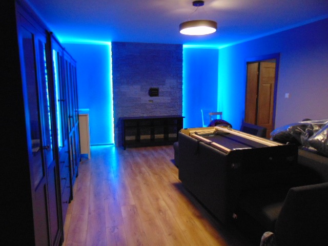 Pokój z podświetleniem LED w kolorze niebieskim, widoczna ściana z kamienia dekoracyjnego, zabudowa meblowa oraz stół bilardowy w trakcie montażu.