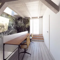 Jasne poddasze z drewnianą konstrukcją stropu, biurkami z drewnianymi blatami i tapetą w motywy roślinne na ścianie, doświetlone oknem balkonowym.