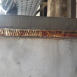 Zbliżenie na świeżo wykonany spaw na metalowej konstrukcji, widoczne charakterystyczne przebarwienia termiczne.