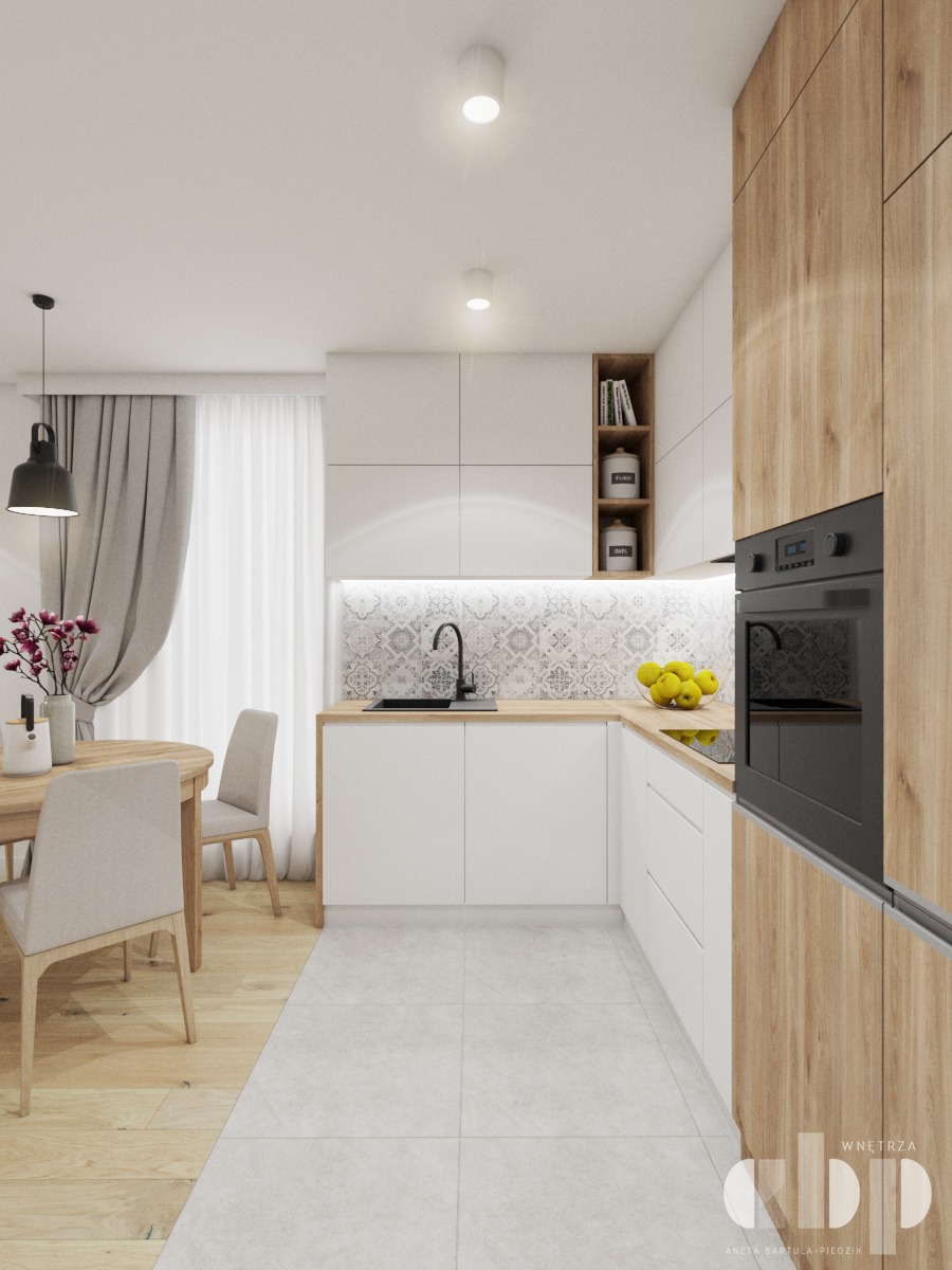 Jasna kuchnia z drewnianymi i białymi szafkami, wzorzystą ścianą nad blatem, okrągłym stołem z kwiatami i szarymi krzesłami, oraz podłogą z płytek przechodzącą w drewniany parkiet.
