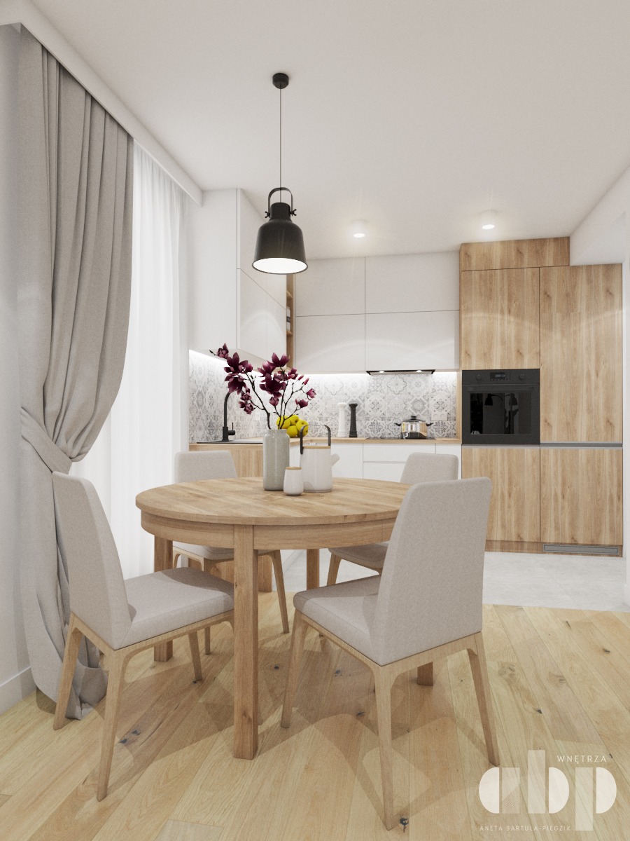 Jasna jadalnia z okrągłym, drewnianym stołem, krzesłami z beżową tapicerką i kwiatami w wazonie, na tle nowoczesnej kuchni z białymi i drewnianymi szafkami oraz czarnym piekarnikiem.