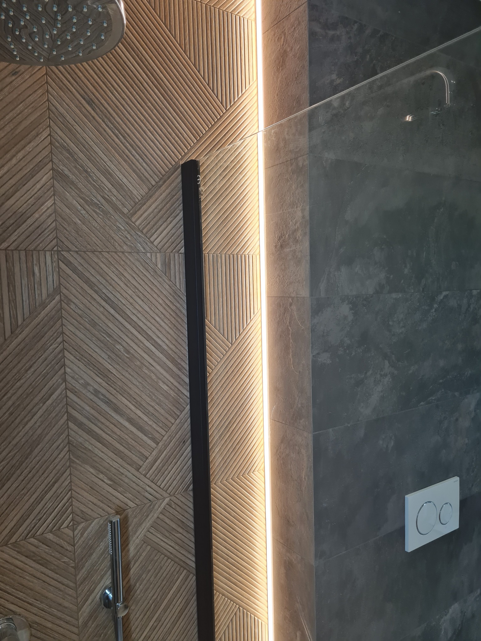 Nowoczesna kabina prysznicowa w Milanówku z drewnopodobnymi płytkami ułożonymi we wzór jodełki, szklana ścianka i panel z przyciskami spłuczki.