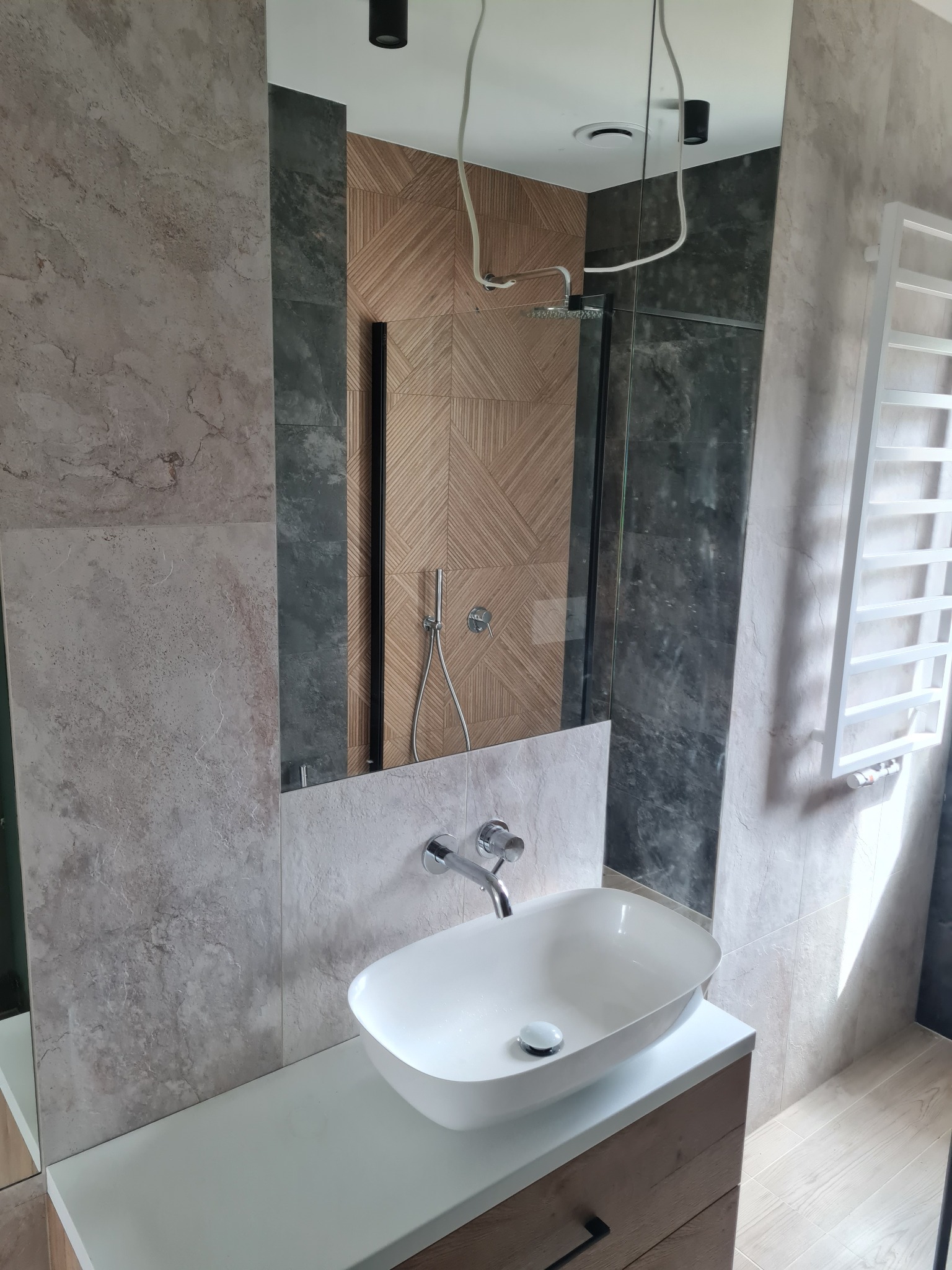 Nowoczesna łazienka z umywalką nablatową, lustrem odbijającym kabinę prysznicową z deszczownicą i dekoracyjnymi płytkami na ścianach.