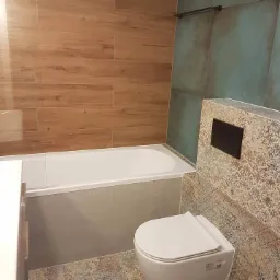 Nowoczesna łazienka z drewnopodobnymi płytkami na ścianie, turkusową ścianą z efektem betonu i wiszącą toaletą z czarnym przyciskiem spłukiwania.