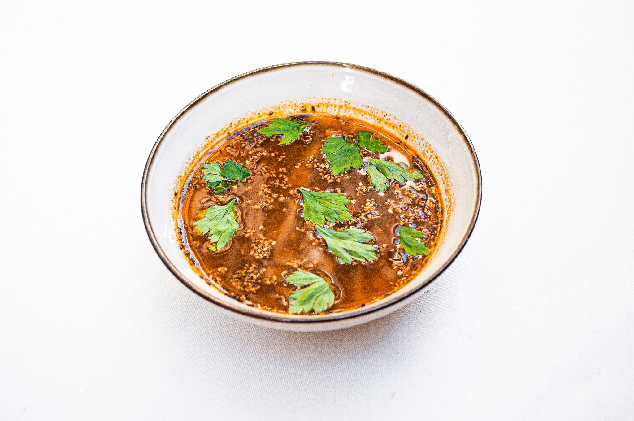 Aromatyczna zupa w ceramicznej miseczce, posypana świeżą zieloną pietruszką, na białym tle.