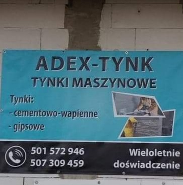 Baner reklamowy firmy Adex-Tynk z ofertą tynków maszynowych cementowo-wapiennych i gipsowych, numerami telefonów i informacją o wieloletnim doświadczeniu, zawieszony na surowej ścianie z pustaków.